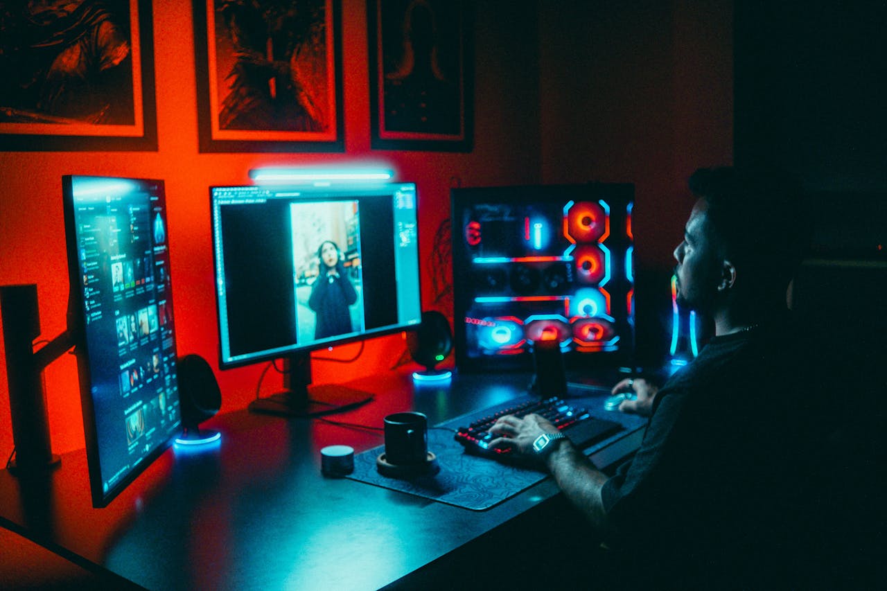 programs-02 A young man working on a multi-screen computer setup in a dark, neon-lit room.